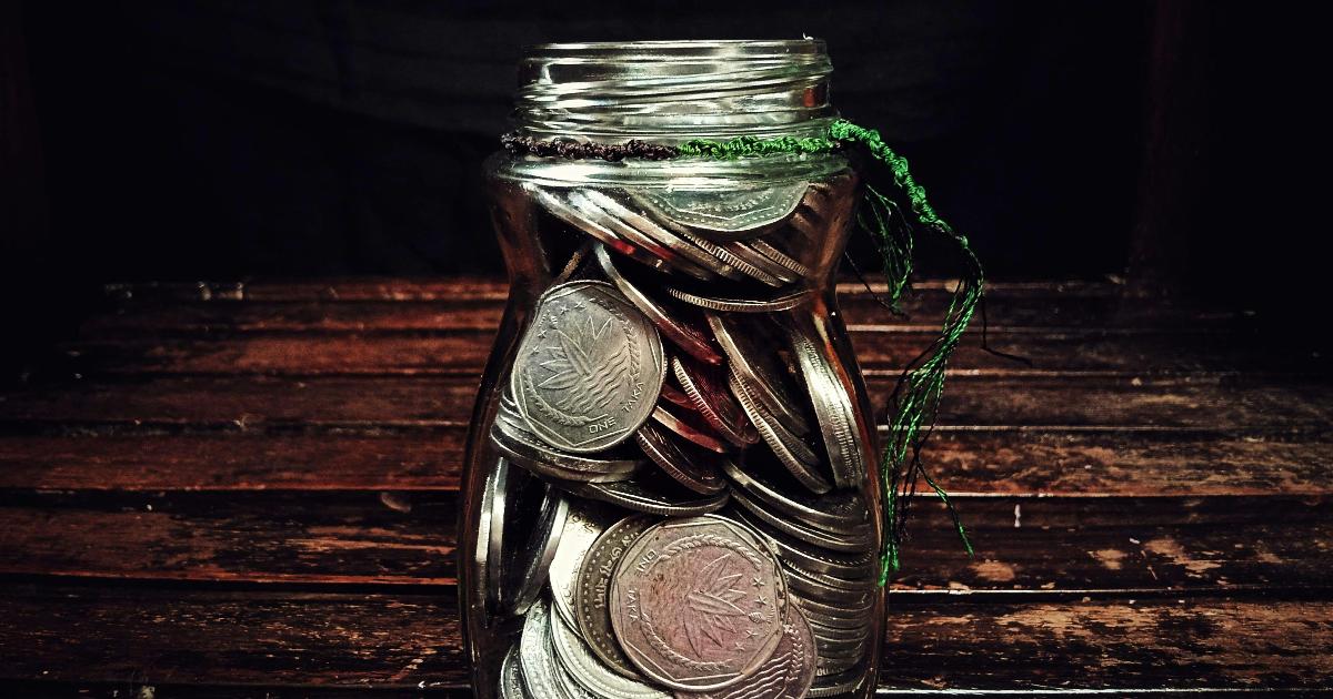 A jar filled with one-dollar bills beside a notebook tracking a $1 savings challenge